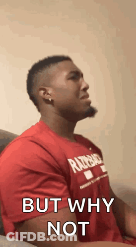 A Man In A Red Shirt Is Sitting On A Couch With His Eyes Closed And Says `` But Why Not '' . GIF