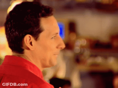 A Man In A Red Shirt Is Smiling And Looking Away From The Camera GIF