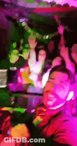 A Man In A Red Shirt Is Smiling In Front Of A Group Of People GIF
