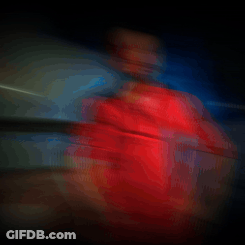 A Man In A Red Shirt Is Standing In A Dark Room With Smoke Behind Him GIF