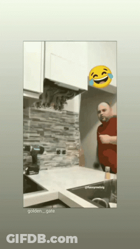 A Man In A Red Shirt Is Standing In A Kitchen With A Yellow Smiley Face Behind Him GIF