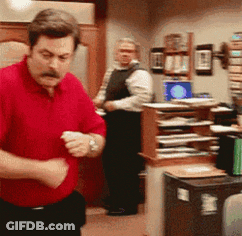 A Man In A Red Shirt Is Standing In A Room GIF