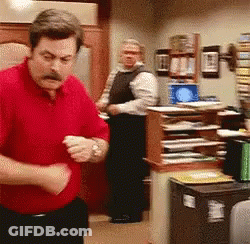 A Man In A Red Shirt Is Standing In A Room With Other Men GIF