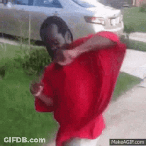A Man In A Red Shirt Is Standing In Front Of A Car . GIF