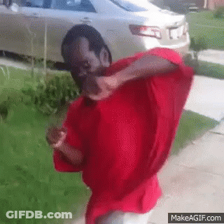 A Man In A Red Shirt Is Standing In Front Of A Car GIF
