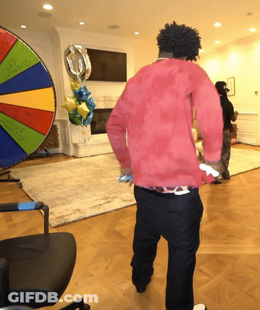 A Man In A Red Shirt Is Standing In Front Of A Colorful Spinning Wheel GIF
