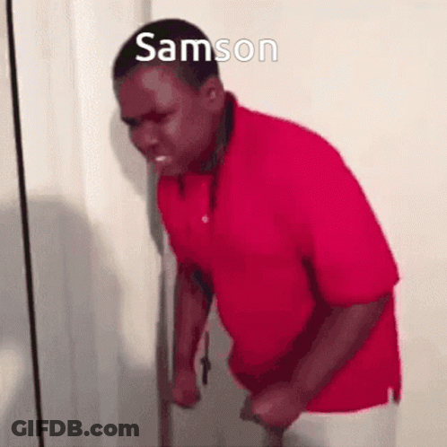 A Man In A Red Shirt Is Standing In Front Of A Door With His Fist In The Air . GIF