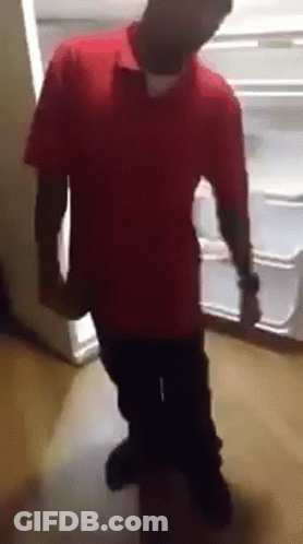 A Man In A Red Shirt Is Standing In Front Of A Fridge GIF
