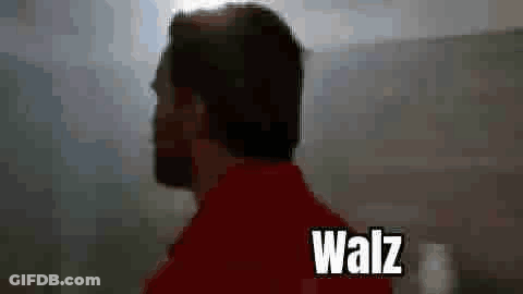 A Man In A Red Shirt Is Standing In Front Of A Mountain With The Word Walz Written On The Bottom . GIF