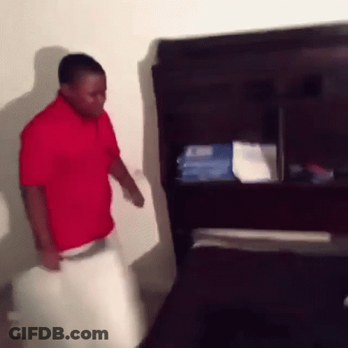 A Man In A Red Shirt Is Standing In Front Of A Television In A Room . GIF