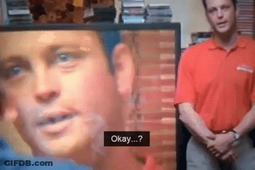 A Man In A Red Shirt Is Standing In Front Of A Tv Screen That Says Okay GIF