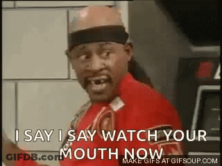 A Man In A Red Shirt Is Standing In Front Of A Wall And Says `` I Say I Say Watch Your Mouth Now '' . GIF