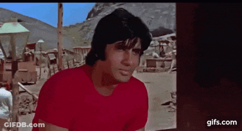A Man In A Red Shirt Is Standing In Front Of A Window . GIF