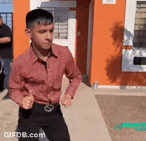 A Man In A Red Shirt Is Standing In Front Of An Orange Building With The Number 505 On It GIF