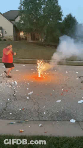 A Man In A Red Shirt Is Standing Next To A Firework Display GIF