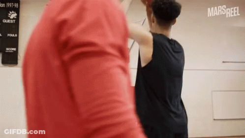 A Man In A Red Shirt Is Standing Next To A Man In A Black Shirt Playing Basketball .. GIF
