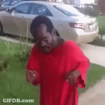A Man In A Red Shirt Is Standing On A Sidewalk In Front Of A White Car GIF
