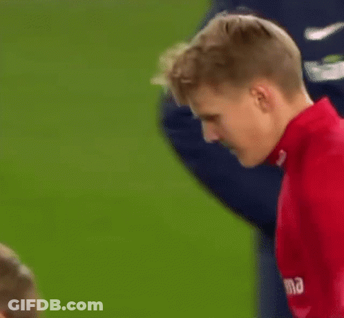 A Man In A Red Shirt Is Standing On A Soccer Field And Looking Down . GIF