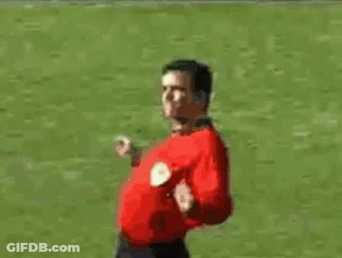 A Man In A Red Shirt Is Standing On A Soccer Field With His Arms Outstretched GIF