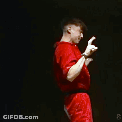 A Man In A Red Shirt Is Standing On A Stage With His Hands Up GIF
