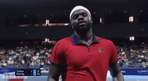 A Man In A Red Shirt Is Standing On A Tennis Court . GIF