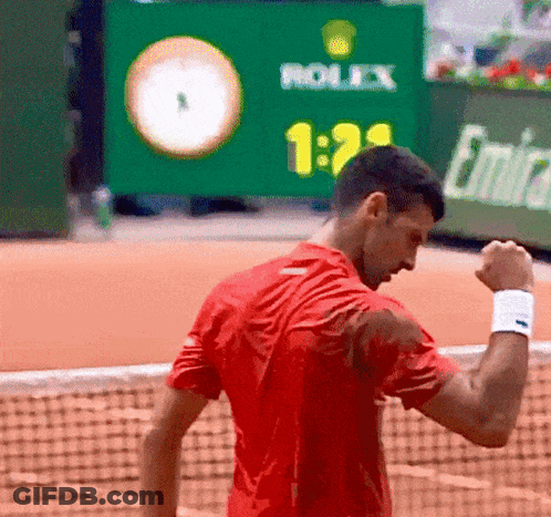 A Man In A Red Shirt Is Standing On A Tennis Court With A Rolex Sign In The Background GIF