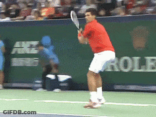 A Man In A Red Shirt Is Swinging A Tennis Racquet GIF