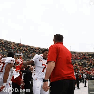 A Man In A Red Shirt Is Talking To A Football Player Wearing A Hoosier Jersey GIF