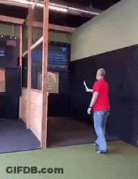 A Man In A Red Shirt Is Throwing An Axe At A Target GIF