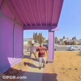 A Man In A Red Shirt Is Walking On A Sidewalk Under A Purple Roof GIF
