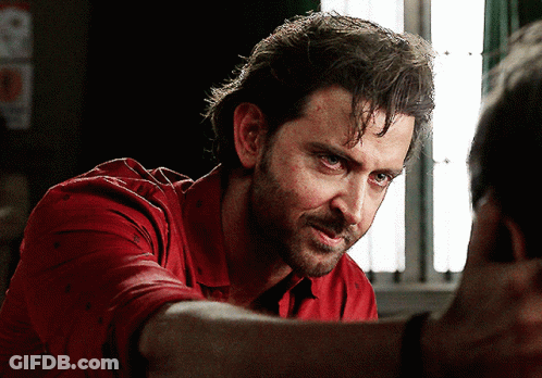 A Man In A Red Shirt Looks Down At Something GIF