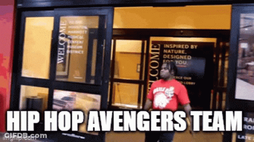 A Man In A Red Shirt Standing In Front Of A Building With The Words Hip Hop Avengers Team GIF
