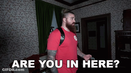 A Man In A Red Shirt Stands In A Room With The Words Are You In Here GIF