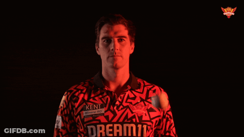 A Man In A Red Shirt Stands In Front Of A Black Background With A Crown On It GIF
