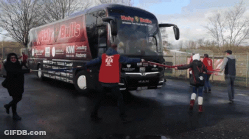 A Man In A Red Shirt Stands In Front Of A Bus That Says Lucky Bulls GIF