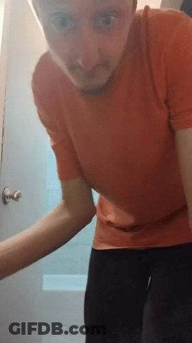 A Man In A Red Shirt Stands In Front Of A Door GIF