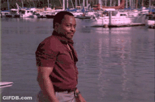 A Man In A Red Shirt Stands In Front Of Boats GIF