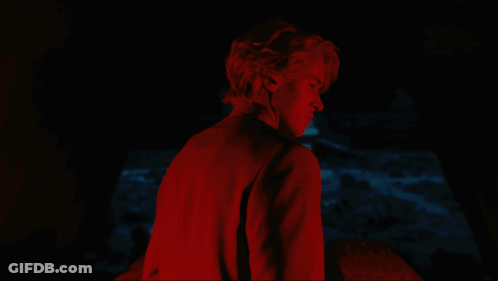 A Man In A Red Shirt Stands In The Dark GIF