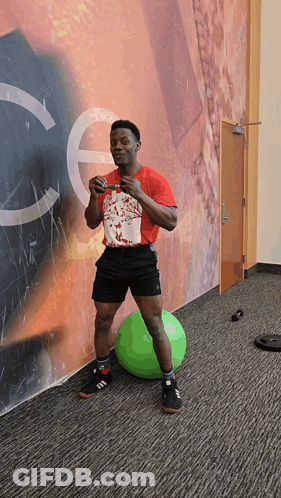 A Man In A Red Shirt Stands On A Green Ball GIF