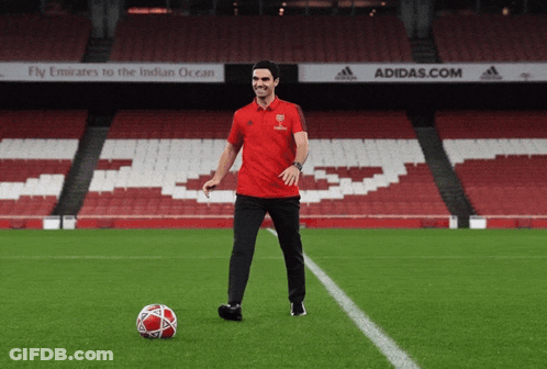A Man In A Red Shirt Stands On A Soccer Field In Front Of A Sign That Says Adidas.com GIF