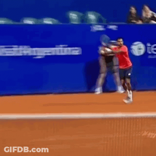 A Man In A Red Shirt Swings A Tennis Racquet On A Tennis Court GIF