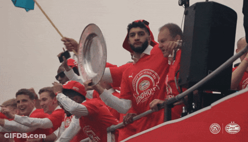 A Man In A Red Shirt That Says ' Psv ' On It Is Holding A Trophy GIF