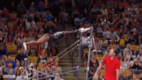 A Man In A Red Shirt Watches A Gymnast Perform On A Bar GIF