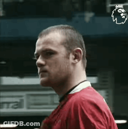 A Man In A Red Shirt With A Crown On His Head Is Standing In Front Of A Building . GIF