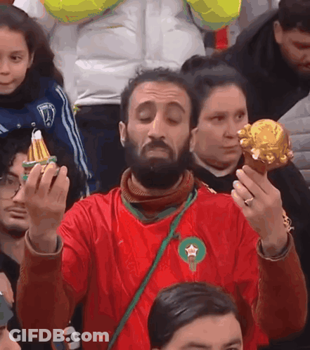 A Man In A Red Shirt With A Green Star On It Holds A Gold Object GIF