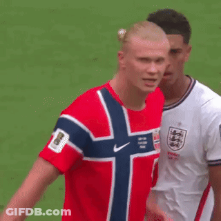 A Man In A Red Shirt With A Norwegian Flag On It Is Standing Next To Another Man In A White Shirt . GIF