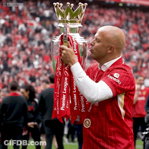 A Man In A Red Shirt With Expedia On It Kisses The Trophy GIF