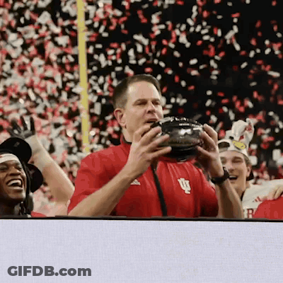 A Man In A Red Shirt With The Letter U On It Holds A Football GIF