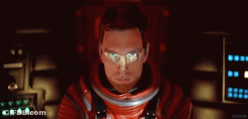 A Man In A Red Space Suit Is Sitting In A Dark Room . GIF