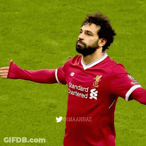 A Man In A Red Standard Chartered Shirt Stands On A Field GIF